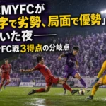 藤枝の選手といわきの選手が雨上がりのピッチで競り合うイメージ。