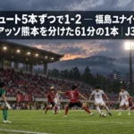曇り空の下、照明に照らされたスタジアムのピッチで両チームがボールを競り合う場面。