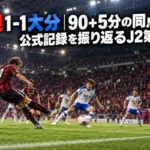 屋内スタジアムの終盤、赤黒のユニフォームの選手がゴール前でシュートを放つ場面