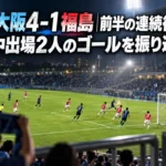 ナイターの照明に照らされたスタジアムで、ゴール前にシュートが飛ぶサッカーの試合風景。