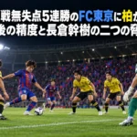 夜のサッカースタジアムで青赤と黄黒のユニフォームの選手がゴール前で対峙するイメージ。